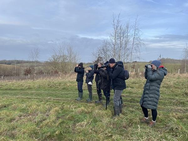 People watching birds through binoculars in a field with trees